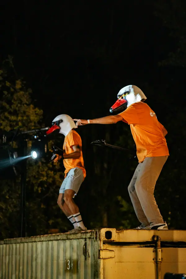 Bénévoles en t-shirt orange et masque d'oie au micro au Belfield Festival 2026