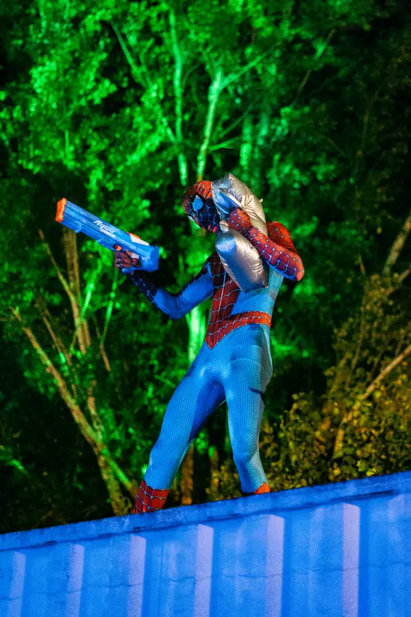 Bénévole costumé en Spider-Man armé d'un pistolet à eau dans la lumière verte du Belfield Festival 2026